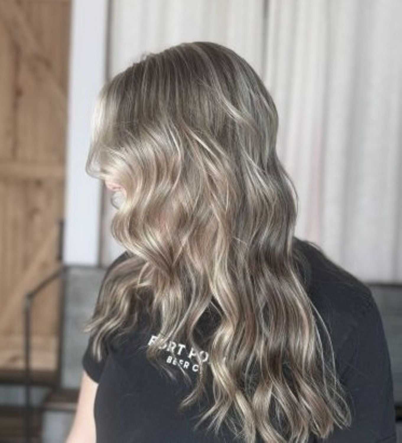 A person with long, wavy, blonde hair in a black shirt, side profile view.